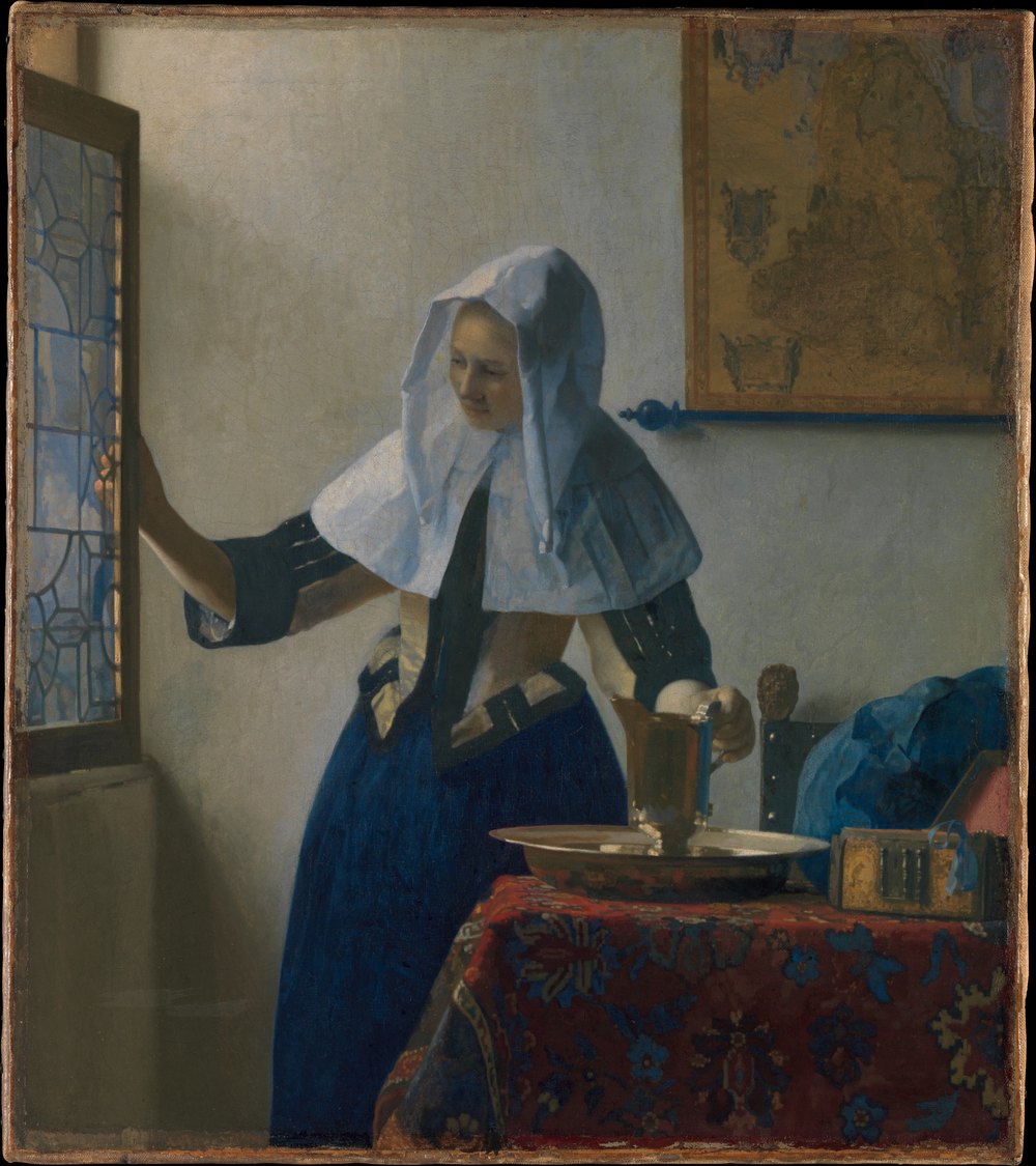 ヨハネス・フェルメール《水差しを持つ若い女》（1662年頃）、メトロポリタン美術館。白い頭巾と襟を着けた女性が、右手で窓を開け、左手で洗面器に置かれた水差しを持っている。背後の壁には地図が掛かる。