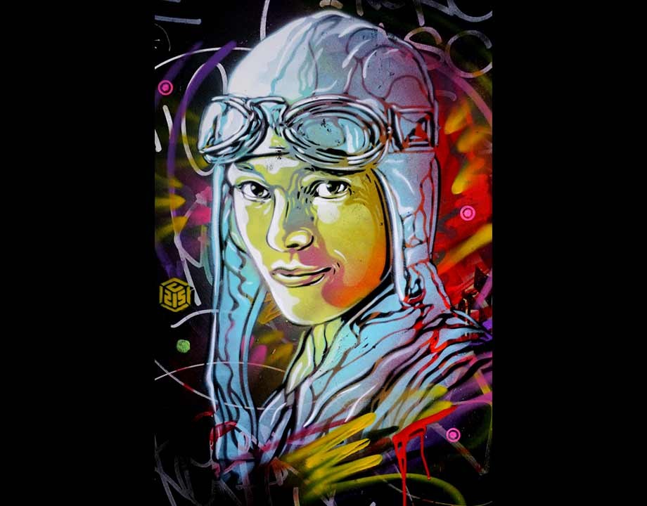 C215によるアメリア・イアハートの肖像。黒い地に、飛行帽をかぶり額にゴーグルを上げた女性の顔が黄色とピンクで描かれ、周りに赤や黄のスプレーの線が走る