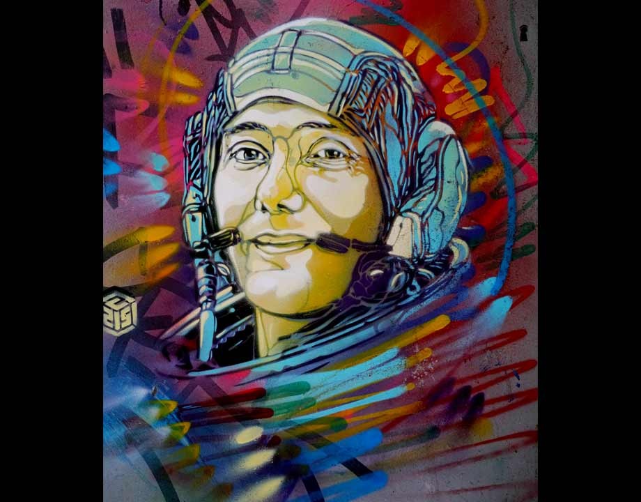 C215によるトマ・ペスケの肖像。ヘルメットをかぶりヘッドセットのマイクを口元につけてほほえむ宇宙飛行士の顔を、青や赤、黄のスプレーの線が渦のように囲む
