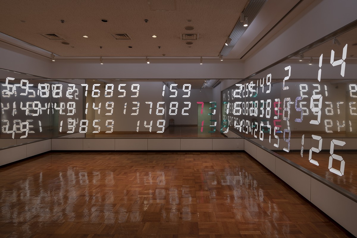 美術館の展示室の壁一面に、数字を切り抜いた鏡のシートが貼られ、白い数字と室内の様子が重なって映り込んでいる。床は木の寄せ木張り。